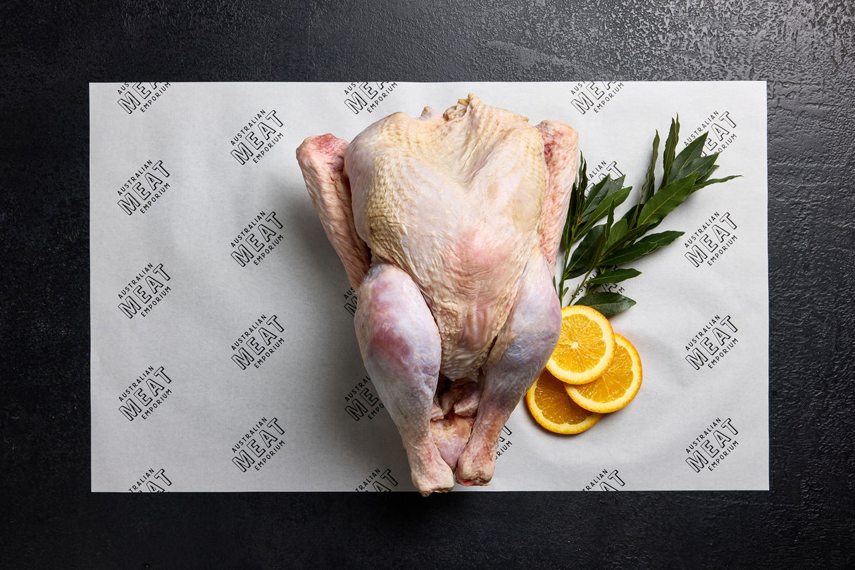 A whole raw turkey displayed on a white paper with the brand name 'Australian Meat Emporium' on it, accompanied by decorative orange slices and a sprig of herbs.