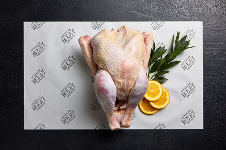 A whole raw turkey displayed on a white paper with the brand name 'Australian Meat Emporium' on it, accompanied by decorative orange slices and a sprig of herbs.